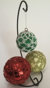 Three baubles coloured red, gold and green with lace coloured red, gold and white respectively