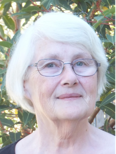 Woman standing in front of tree leaves, grey hair, wearing glasses