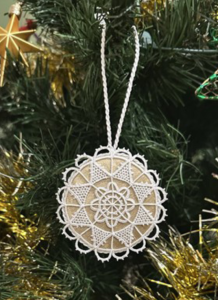 Circular Reticella lace piece attached to light brown paper or similar, hanging on Christmas tree branch