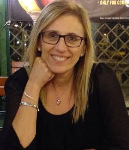 Woman with blonde hair, dark rimmed glasses, smiling at camera, wearing a black top